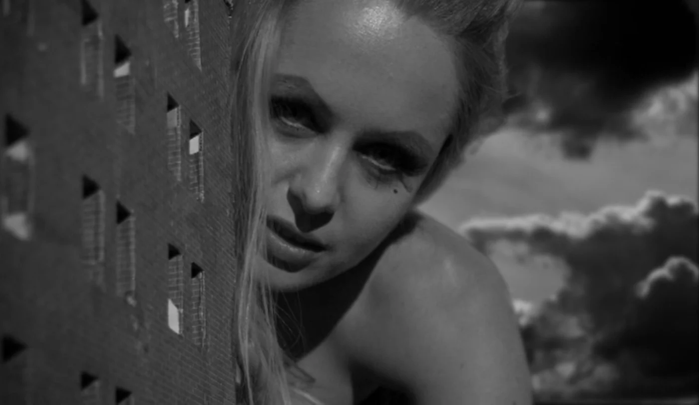 Black-and-white Swingers still of a face emerging beside a miniature building
